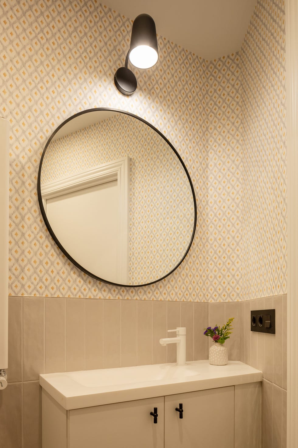 baño con papel pintado con motivos geométricos y espejo redondo