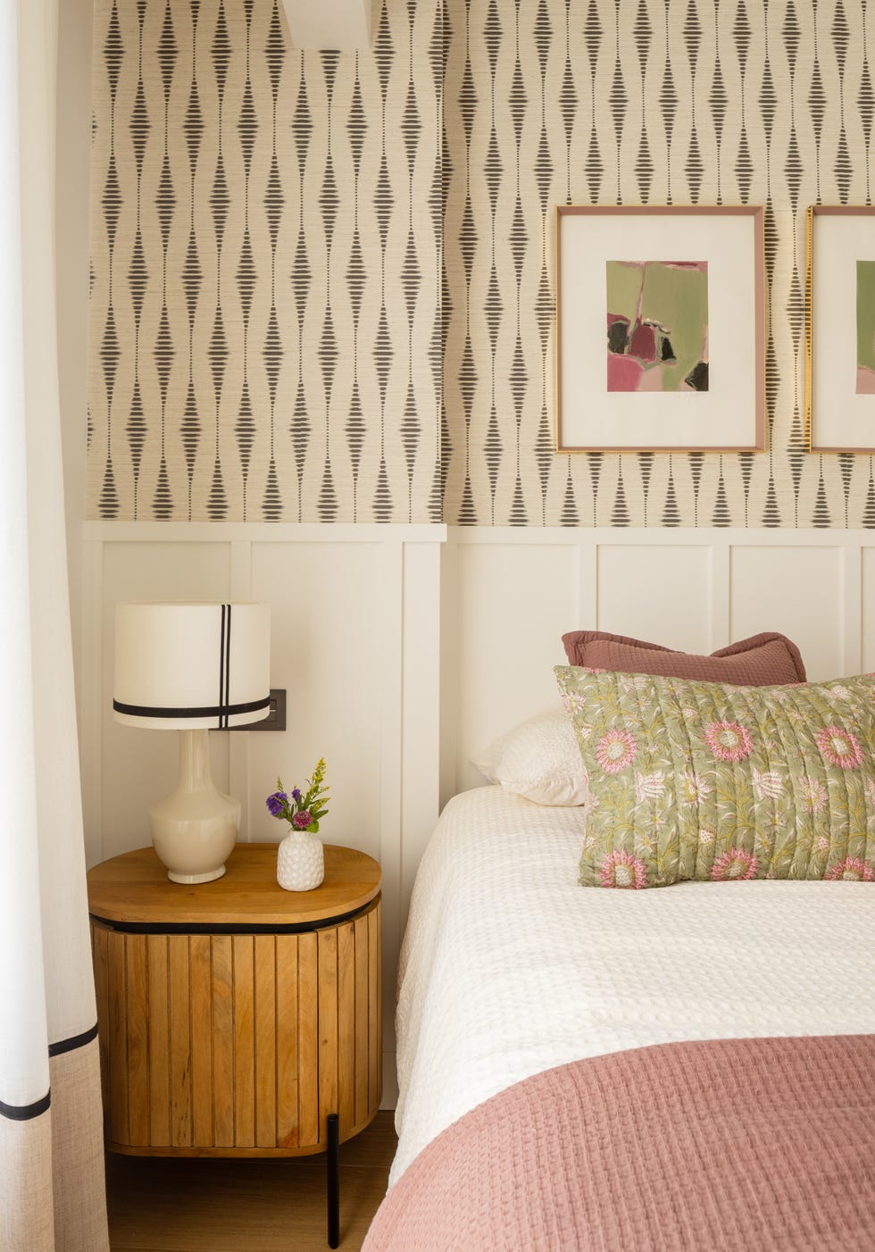 dormitorio con arrimadero de madera blanco, papel pintado con motivos geométricos y mesita de madera con lámpara de mesa