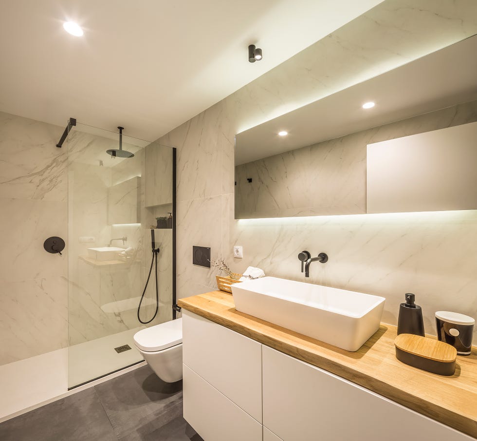 baño con ducha de obra, paredes de mármol y mueble de lavabo suspendido