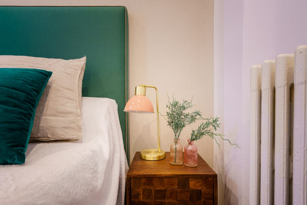 cabecero tapizado en verde, mesita de noche de madera y lámpara de mesa rosa y dorada