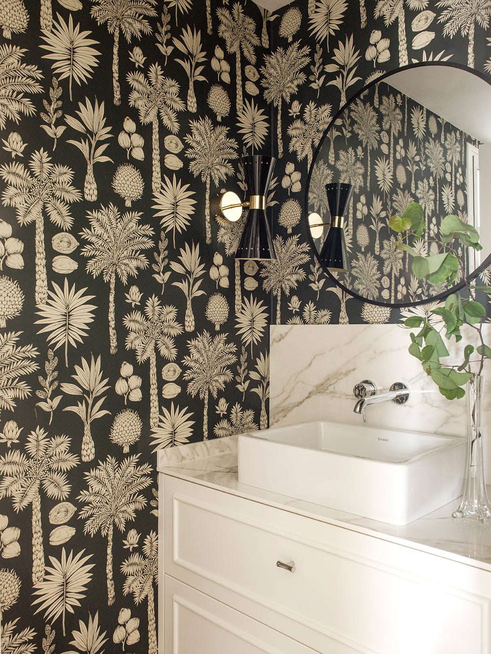baño con mueble blanco y encimera de mármol y papel pintado con motivos exóticos