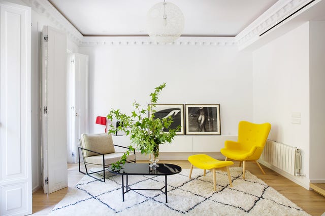 salón señorial con butaca orejera con reposapiés de color amarillo, mesa baja negra ovalada y sillón con estructura metálica negra y cojín beige