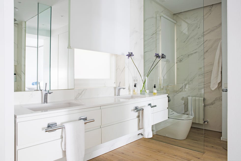baño con mueble de color blanco suspendido con dos lavabos y revestimientos de mármol