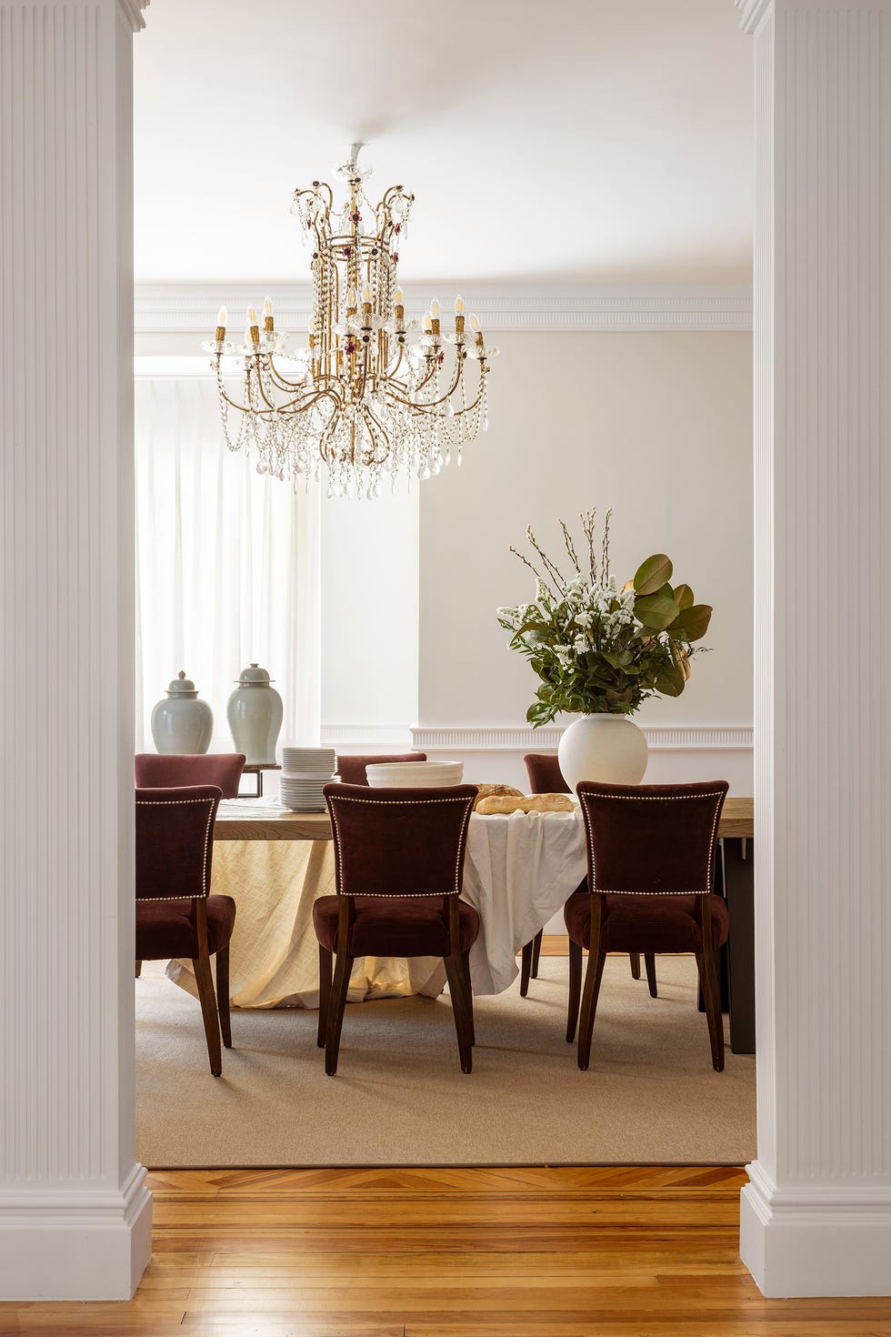 comedor clásico con sillas de terciopelo burdeos, mesa de madera y metal y lámpara de araña