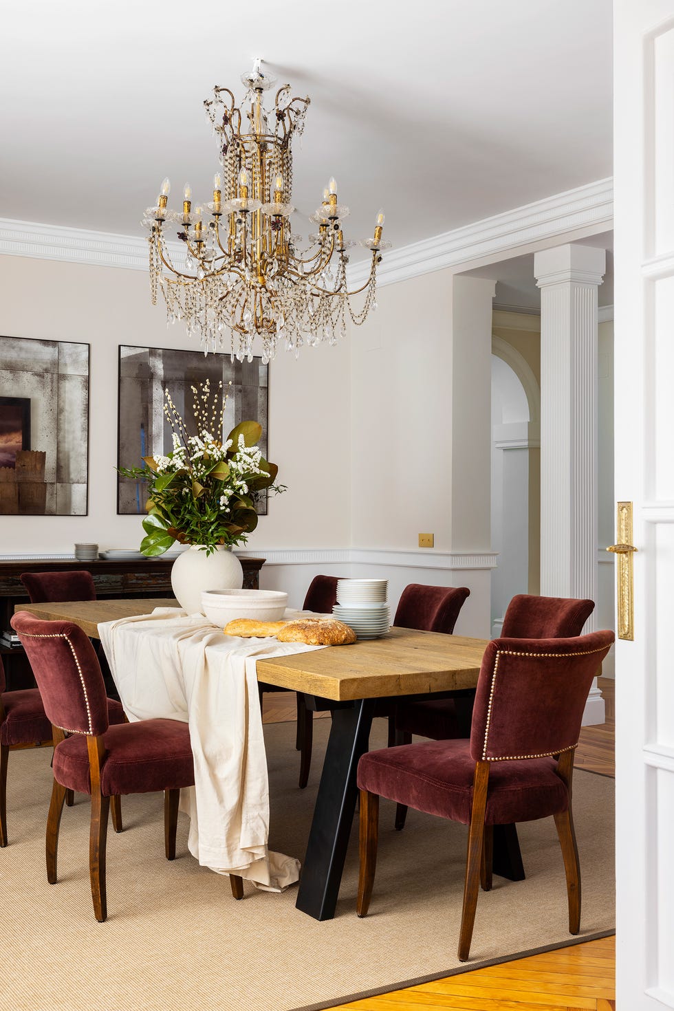 comedor clásico con sillas de terciopelo burdeos, mesa de madera y metal y lámpara de araña