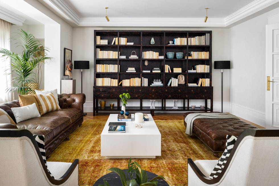 salón de diseño con plantas de interior, sofá chester y puf a juego, mesa de centro blanca moderna y librería antigua