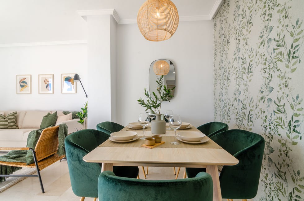 comedor con mesa de madera, sillas de terciopelo verde y papel pintado con motivos botánicos