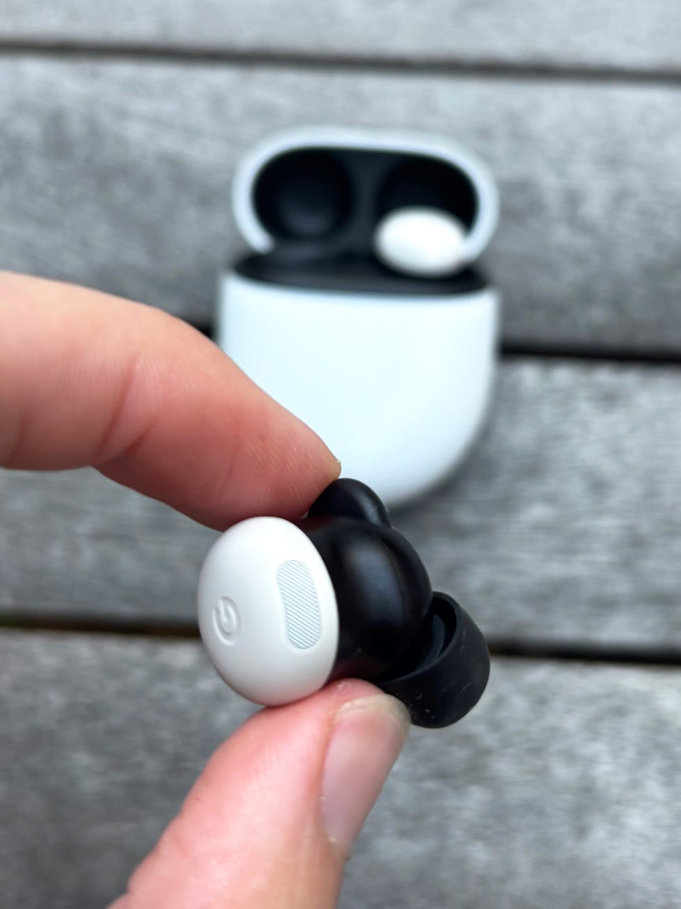 wireless earbud being held with charging case in background