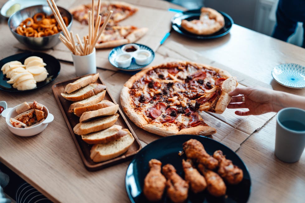 high angle view of a female hand holding a slice of pizza. various food freshly served on the dining table.