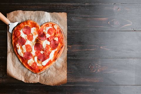 pizza in the shape of heart. lying on a paper for a baking and wood table made of ebony