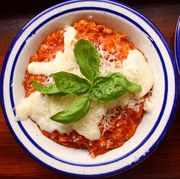 a bowl of red tinged tomato based "pizza" flavored oatmeal topped with mozzarella and parmesan, with a sprig of basil