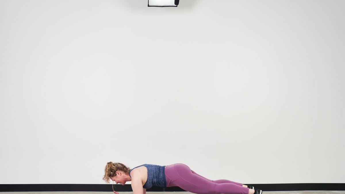 Slim woman in sportswear looking at camera while doing plank on