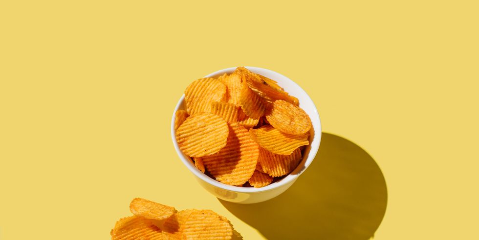 plate of potato chips on yellow background flat lay, top view, copy space