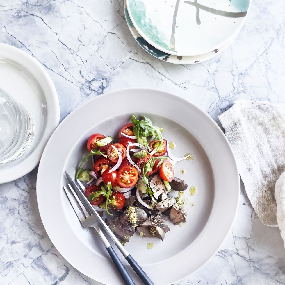 plate of roasted chicken liver with tomato salad on white, marble background