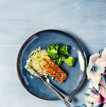 a plate of roasted salmon, rice cauliflower, broccoli and salad on white, blue background