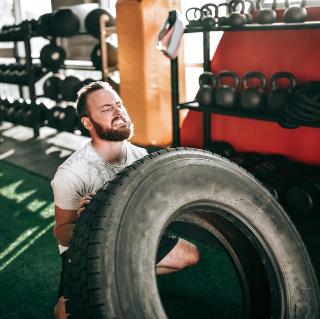 sweaty male athlete doing truck tire training in gym