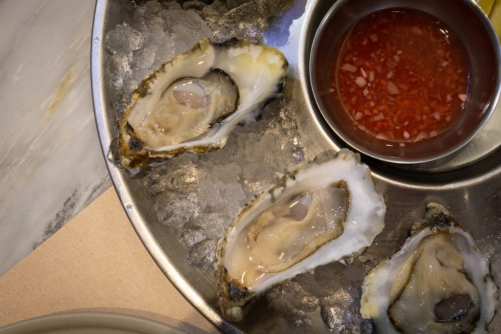 a platter of fresh organic raw oysters on ice with mignonette sauce on the table