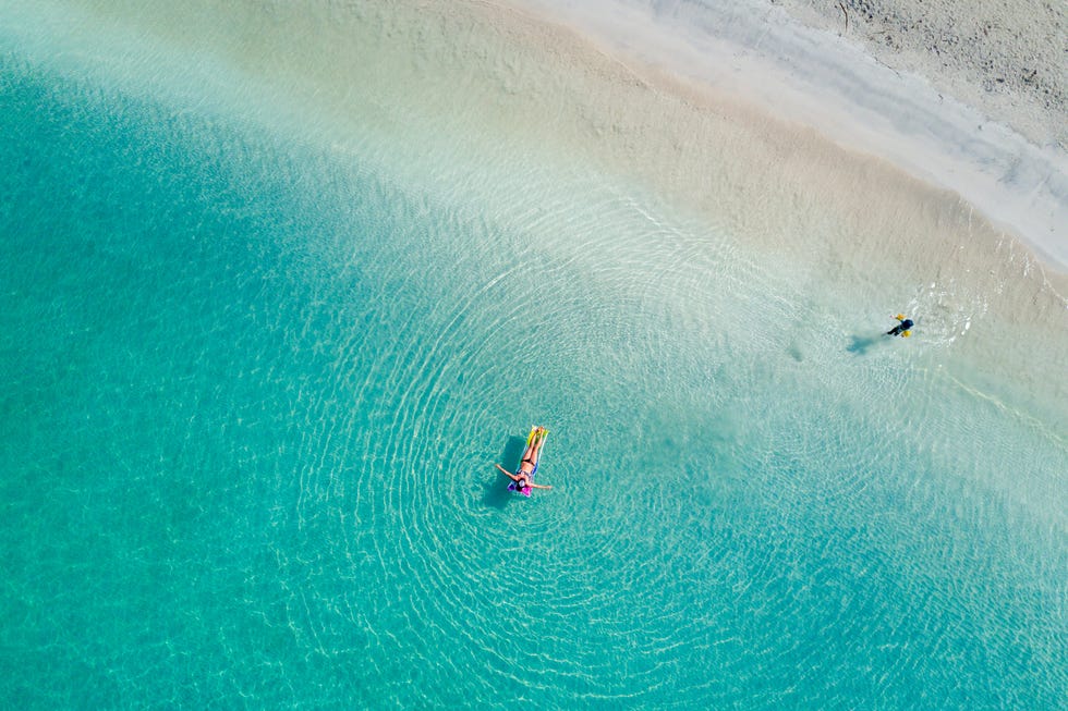 overhead view of two people in turquoise water along a white sand beach