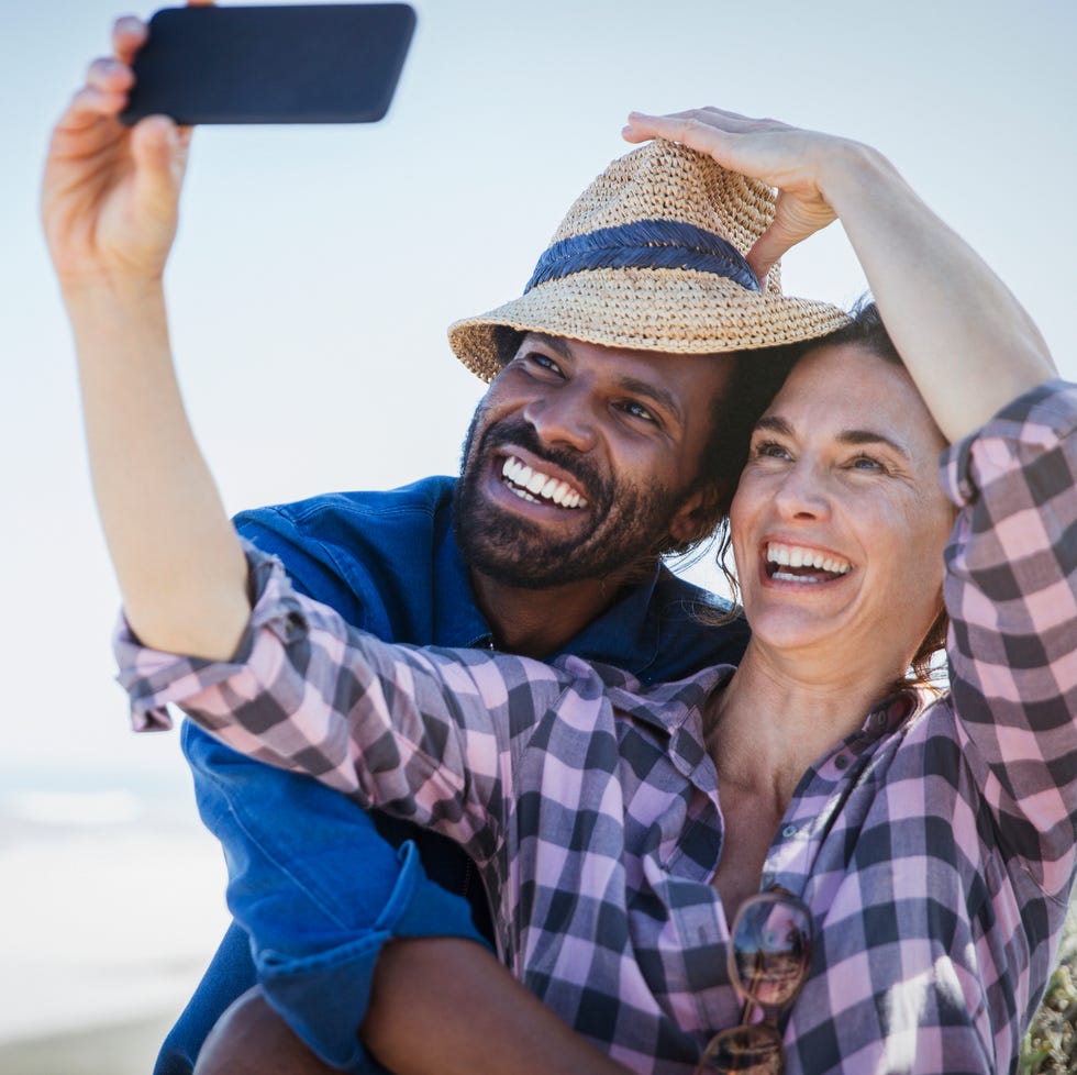 Playful, smiling multi-ethnic couple taking selfie with camera phone on sunny summer beach