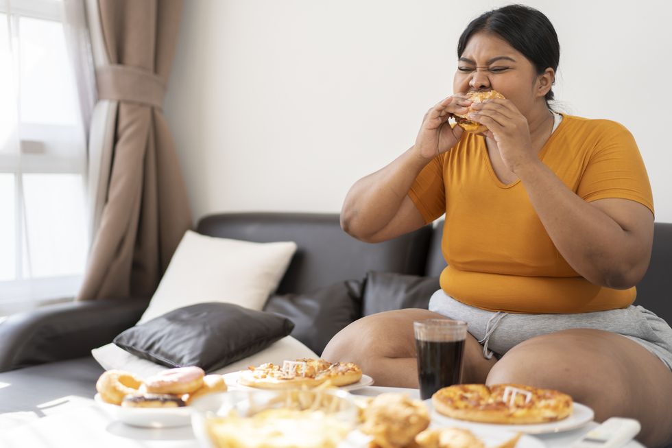 plus size woman sitting on sofa and eating junk food