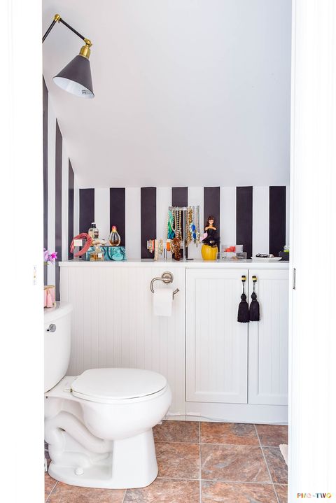 bathroom with bold black and white striped walls, jewelry box in blue and black swirling design sitting on a counter with acrylic necklace and bracelet holders on a counter with a barbie doll on it