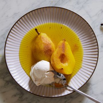 golden yellow poached pears in poaching liquid with vanilla ice cream on a pink plate