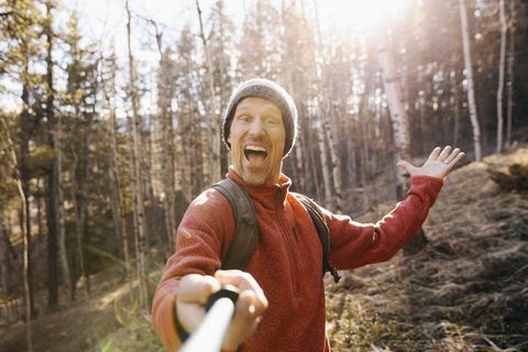 Point of view man hiking, taking selfie with selfie stick in sunny woods