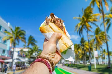 pov point of view shot of a young travel male enjoying his vacations while eating a cuban sandwich in front of ocean drive, south beach, miami beach, miami, south florida, united states of america