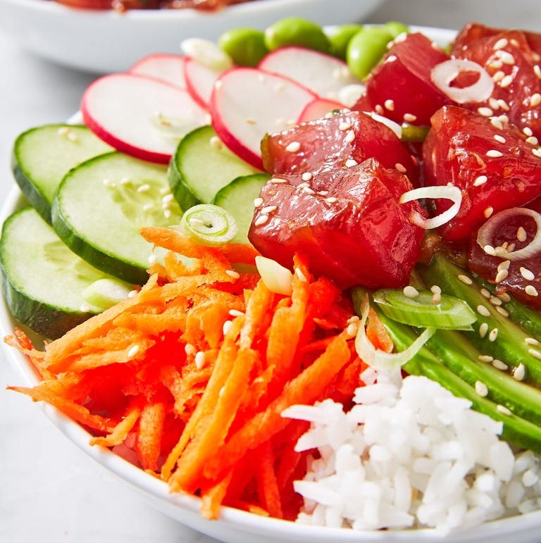 closeup of poke rice bowl with tuna, carrots, cucumber, radish, edamame, and scallions