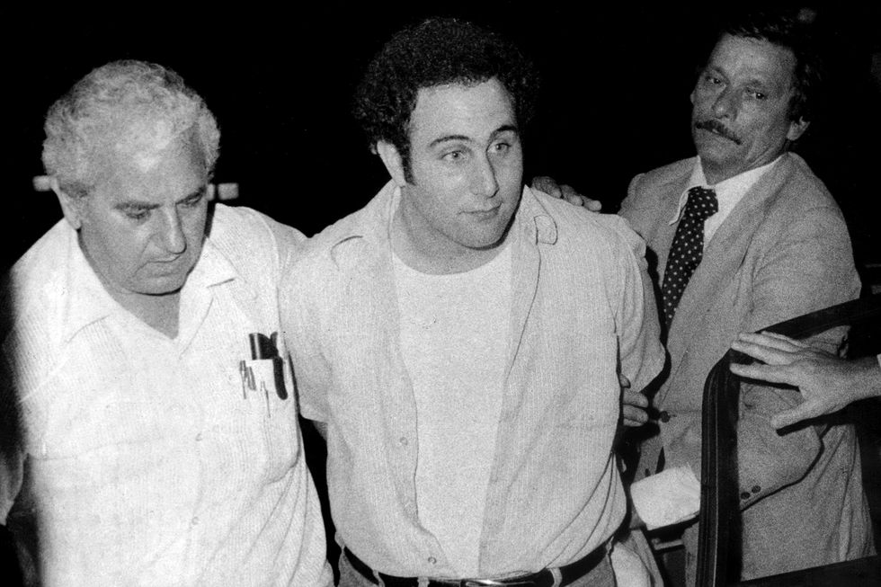 three men walk together, the man in the middle is escorted with his hands behind his back