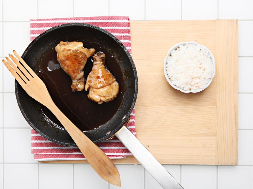 muslos de pollo cocinados en una sartén con un cuenco de arroz blanco al lado