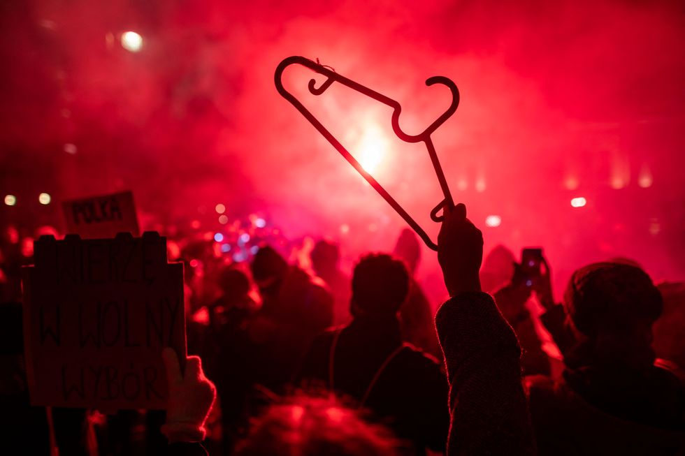 a demonstrator holds up a cloth hanger as others light flares during a pro choice demonstration in front of the constitutional court in warsaw, poland, on january 28, 2021, as part of a nationwide wave of protests since october 22, 2020 against polands near total ban on abortion   hundreds of poles rallied in warsaw against a controversial court verdict imposing a near total ban on abortion protesters also took to the streets elsewhere in the eu member in what was the second night of outrage after the constitutional court ruling came into effect on wednesday, january 27, 2021 photo by wojtek radwanski  afp photo by wojtek radwanskiafp via getty images