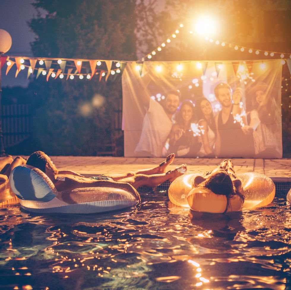 group of people watching a movie while sitting in inflatables in the pool at night
