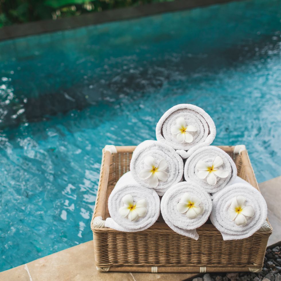 set of rolled white beach towels in wicker box on poolside, decorated with tropical flowers