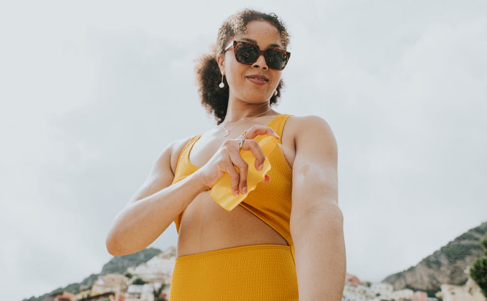 woman wearing sunglasses, spraying sunscreen on to her arm