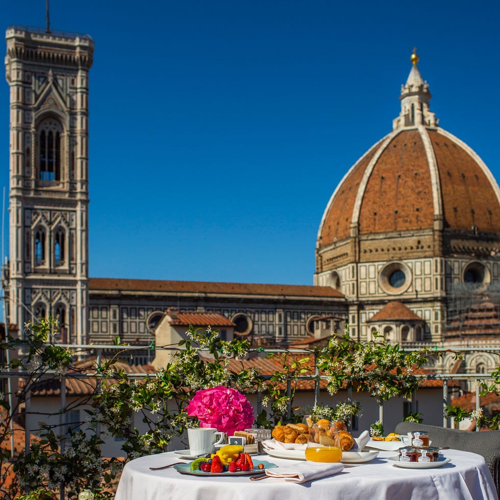 hotel brunelleschi pool suite with table set out on the terrace overlooking the duomo cathedral, with an elaborate breakfast spread including fruit and croissants on it