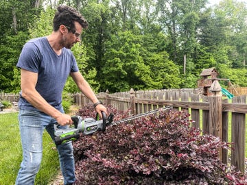 a man using a ego power+ 26 inch electric hedge trimmer on a bush