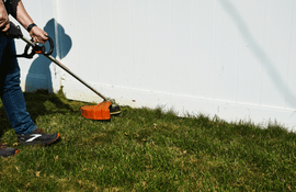 a person using a string trimmer along a white fence