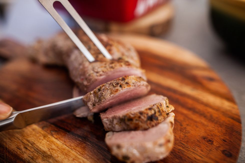 cette photographie présente une personne en train de découper un morceau de viande en tranche à l'aide d'un pique et d'un couteau