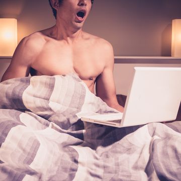 Young man in bed watching pornography on laptop