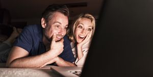 Amazed mature couple lying on couch at home looking at laptop