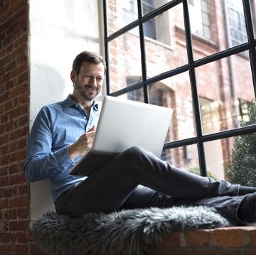 un hombre con un ordenador portátil de apple al lado de una ventana
