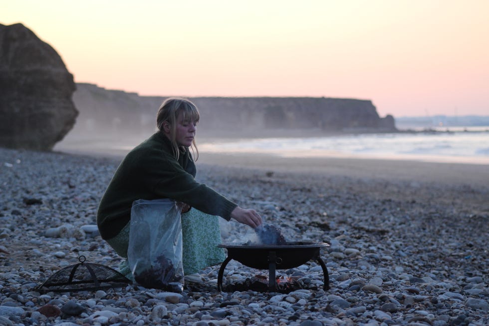 person tending to a fire pit on a beach during sunset