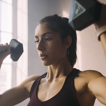 portrait of a beautiful caucasian woman doing arm and shoulder exercises with dumbbells (violet background)