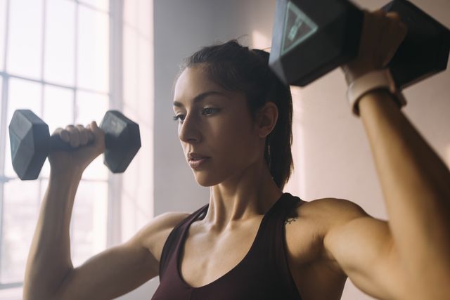 portrait of a beautiful caucasian woman doing arm and shoulder exercises with dumbbells (violet background)