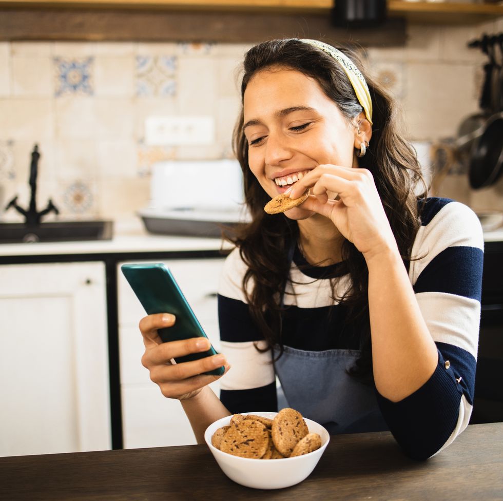 portrait of a beautiful girl having fun online while snacking cookies.