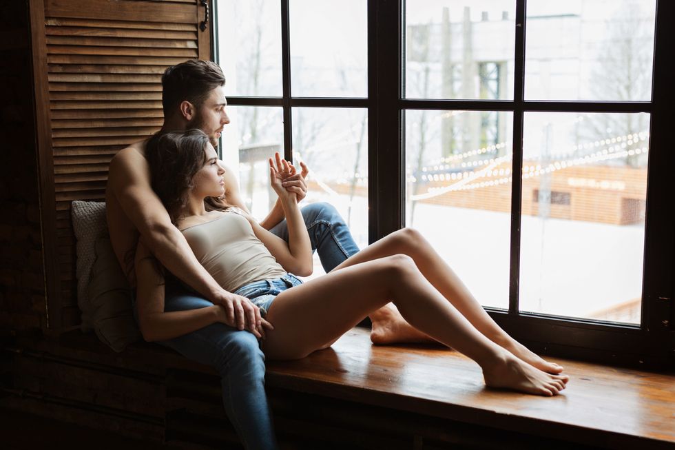 portrait of a charming young couple at home man is embracing his girlfriend near window two people relaxing together