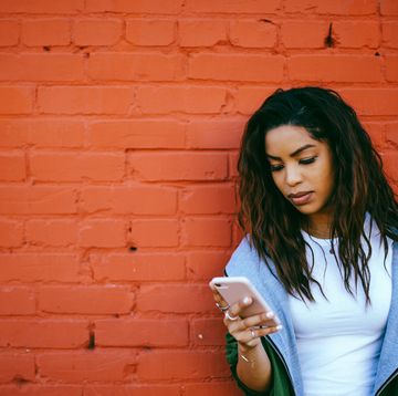 woman looking pensively at smartphone against brick wall