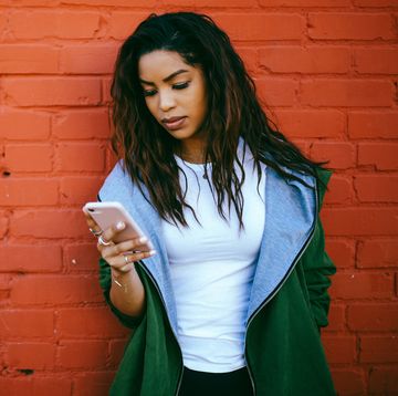 woman looking pensively at smartphone against brick wall