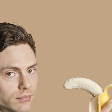portrait of a mid adult man holding banana over colored background